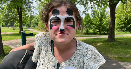 A white teenage girl is standing outside and has her face painted like a panda