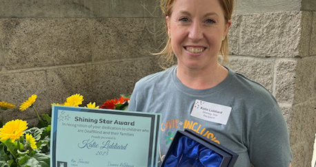 A white woman with brown hair is standing outside with flowers and smiling