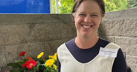 A white woman with brown hair is standing outside with flowers and smiling
