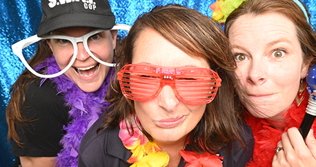 Three white, middle aged women are wearing costume props and making silly faces for the photo booth picture